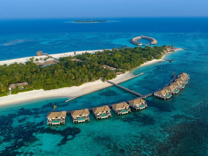 The island and its row of water villas over the reef, from the air