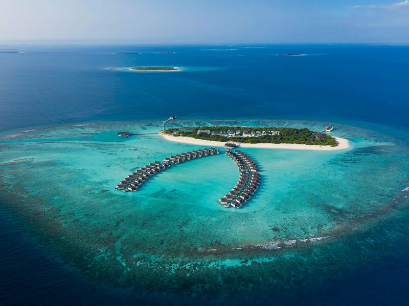 The island and its two arcs of overwater villas, from the air