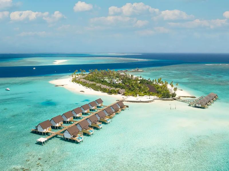 The island, its beach and overwater villas, from the air