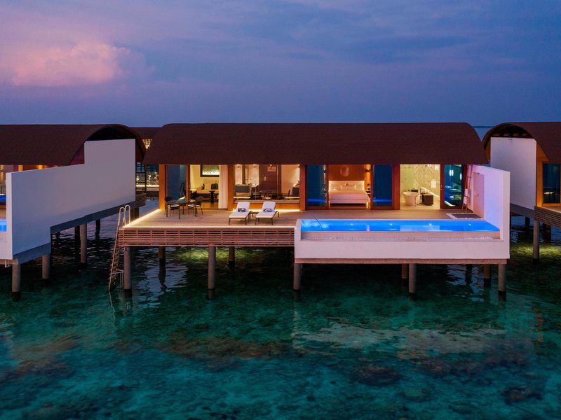 An overwater pool villa lit up at dusk