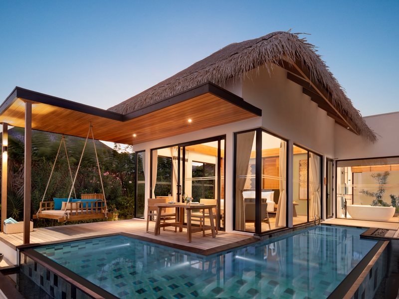 A beach pool villa at dusk, with a hanging swing bed