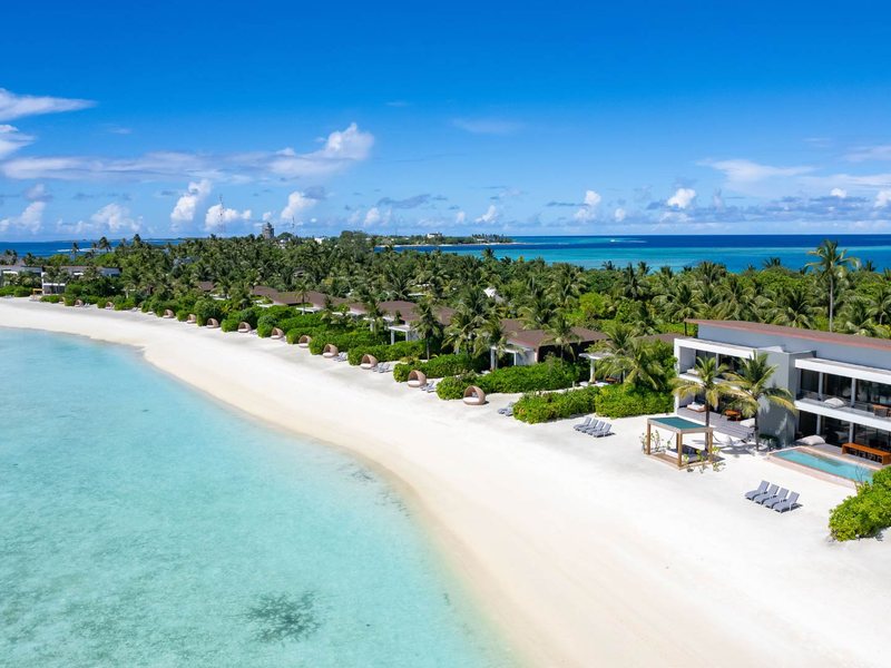 Beach villas with pools along a curving white beach, from the air