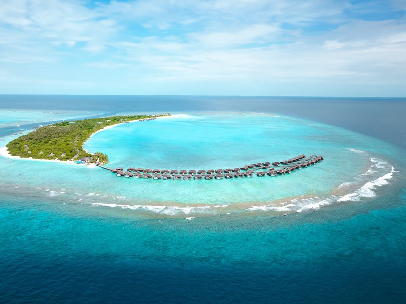 The island and its arc of overwater villas, from high above