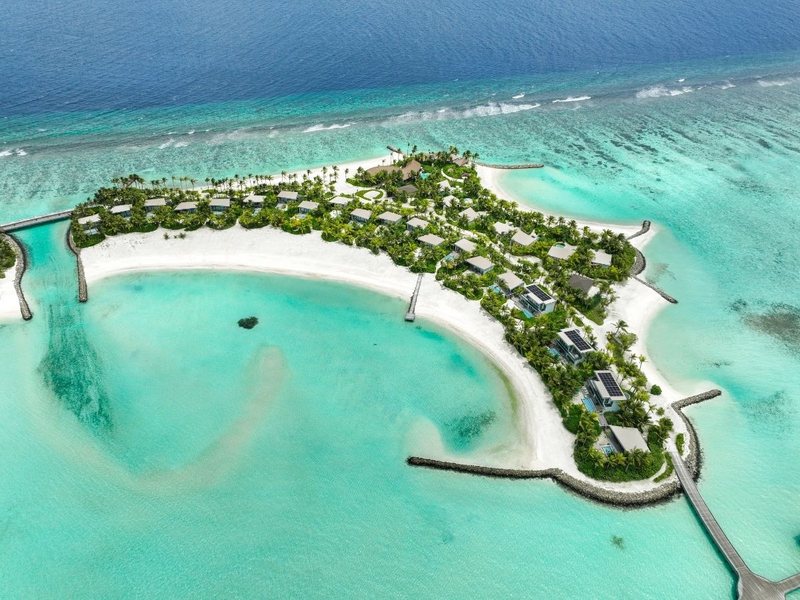 The island’s curving beach and lagoon, with villas among the palms, from the air