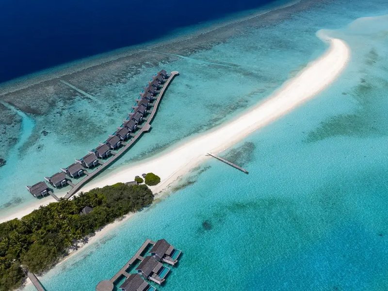 A long white sandbank reaching past the overwater villas, from the air