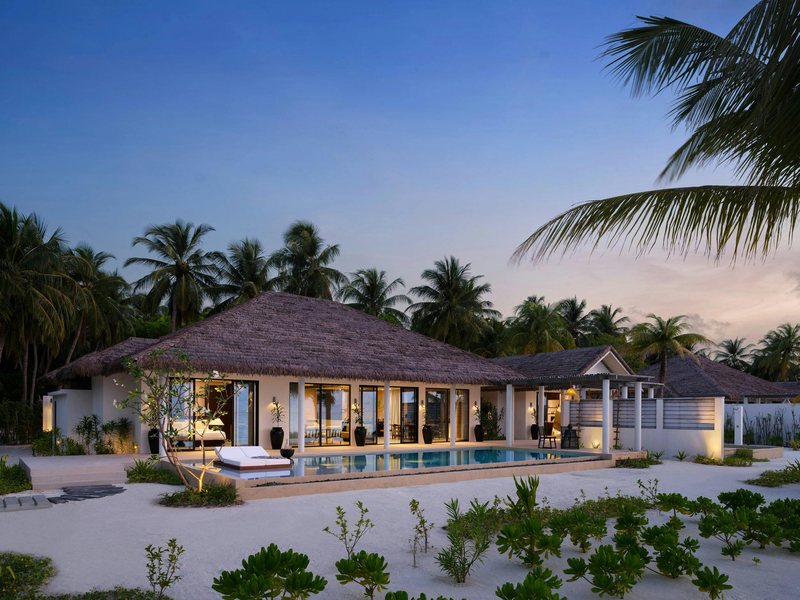 A residence and its pool lit on the beach at dusk