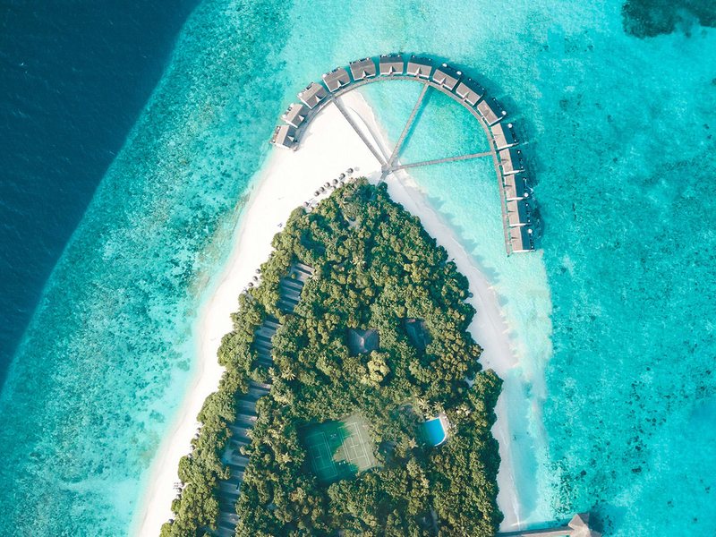 The island and its arc of overwater villas, from high above