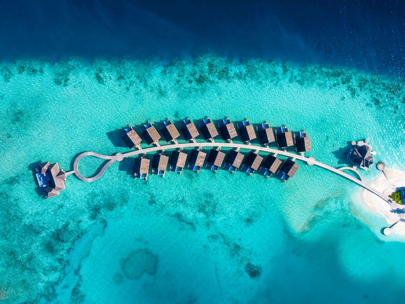 A curve of overwater villas over the reef, from high above