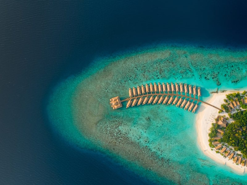 An arc of water villas on the reef edge, from high above