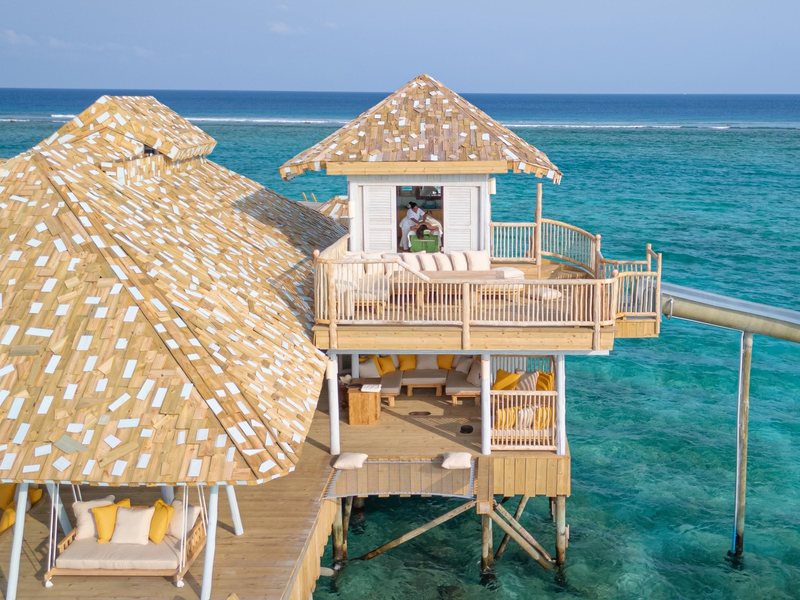 An overwater villa with timber-shingle roofs and a slide, from the air