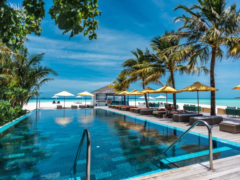 A pool lined with palms and parasols beside the beach