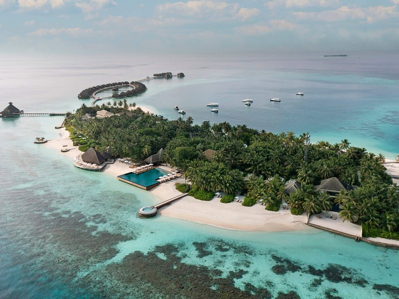 The island, its beach and overwater villas, from the air