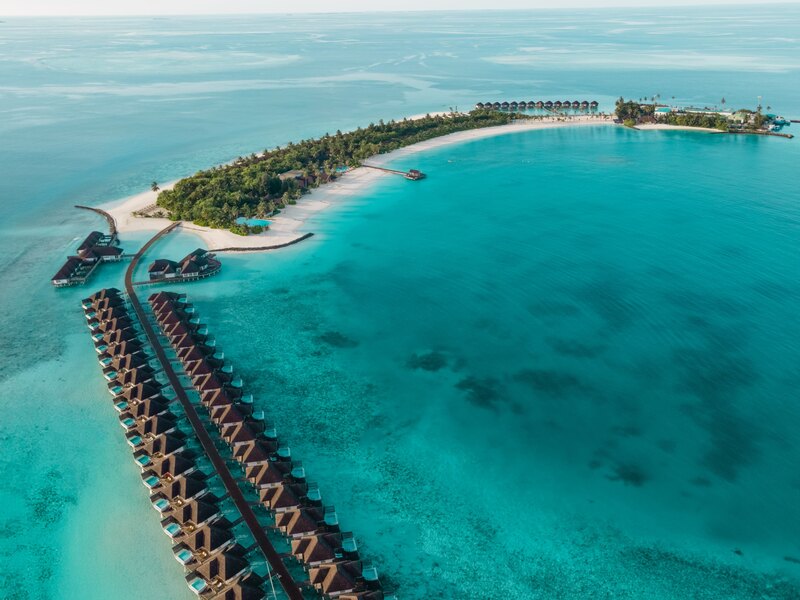 The island and a long row of overwater villas, from the air