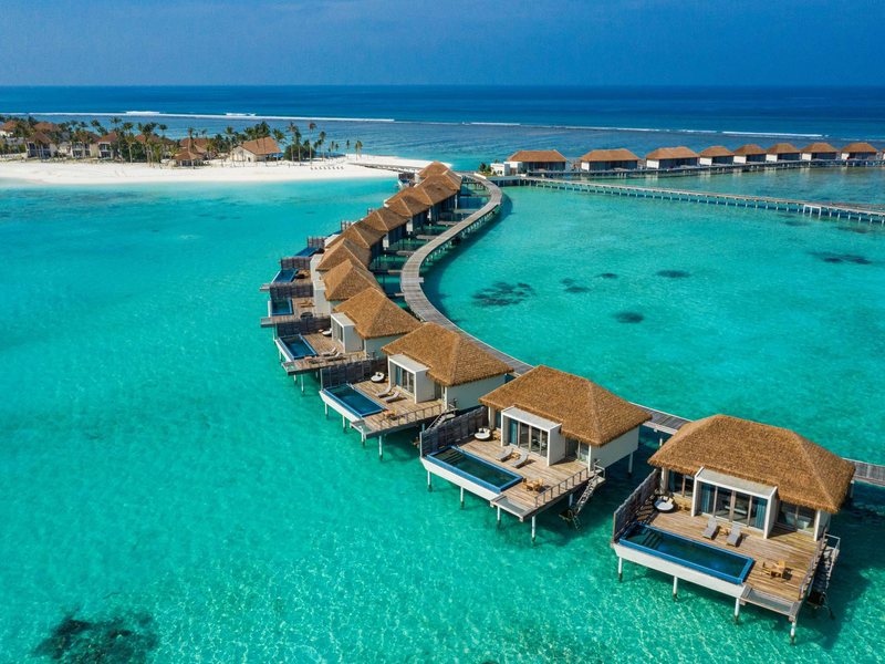 A curving row of thatched overwater villas, each with a pool