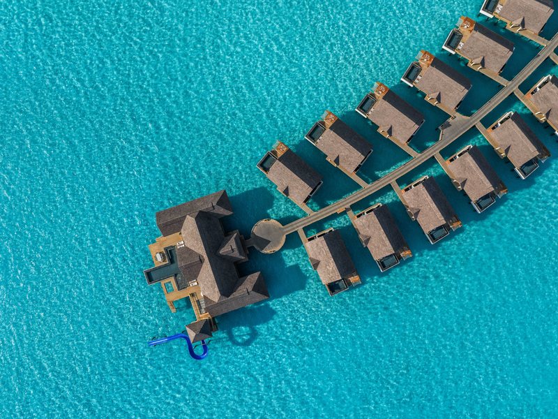 Overwater villas along a jetty, with a larger residence at the end, from above