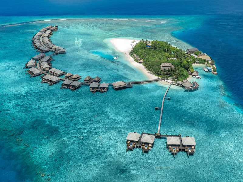 The island and its arcs of water villas over the reef, from the air