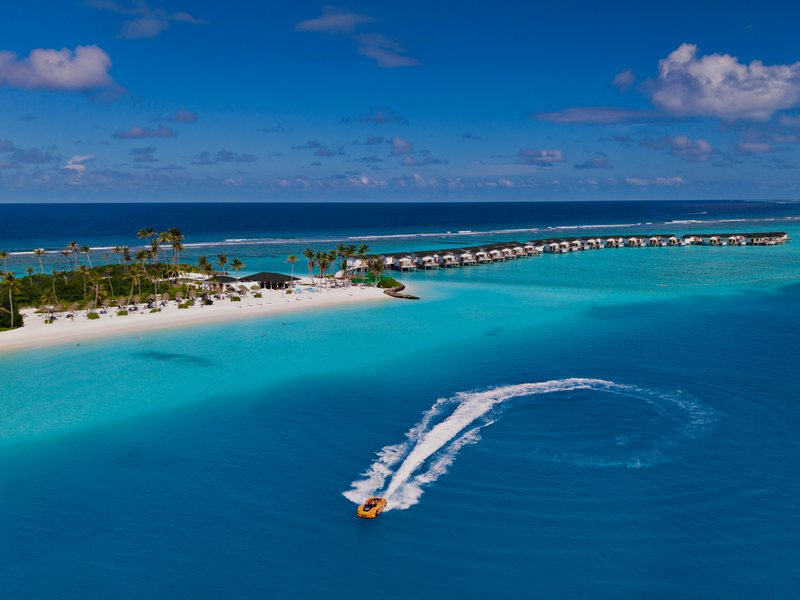 A speedboat curving past the island and its water villas