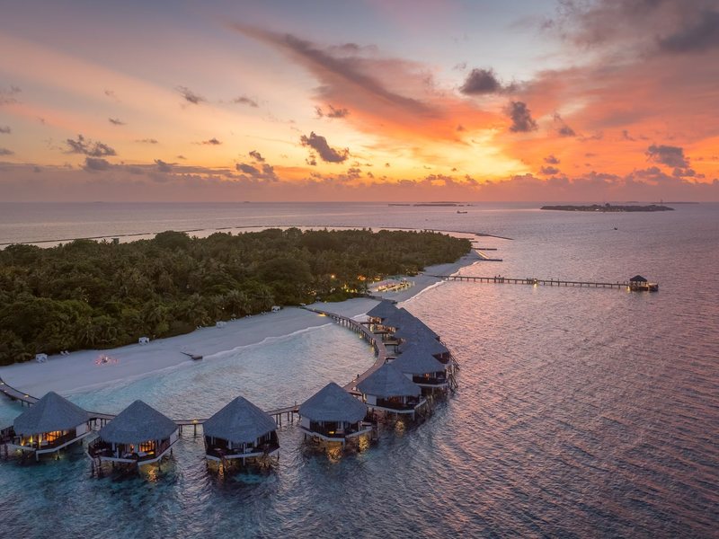 An arc of water villas at sunset, with the island behind