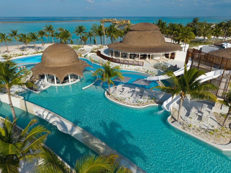 A pool complex with water slides and thatched dome pavilions among palms, from the air
