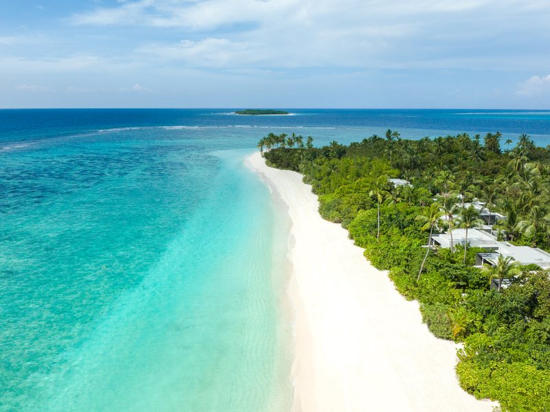A long white beach beside the forested island, from the air